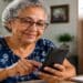 Mulher idosa usa o celular para se inscrever no CadEJA, plataforma do MEC para a Educação de Jovens e Adultos, ao lado do logo do programa.