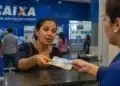 Mulher recebendo cédulas em atendimento na Caixa, representando os depósitos de R$ 300 para 100 mil mulheres em julho.