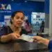 Mulher recebendo cédulas em atendimento na Caixa, representando os depósitos de R$ 300 para 100 mil mulheres em julho.