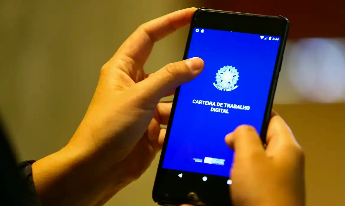 Abono Salarial PIS/Pasep 2026 Pessoa acessando o aplicativo Carteira de Trabalho Digital em smartphone para consulta de direito ao abono salarial.