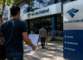 Candidato a concurso público em frente à Receita Federal segurando documento de inscrição ou prova.