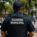 Guarda municipal fardado de costas em área urbana, representando o concurso da Guarda Municipal de Balneário Piçarras (SC).
