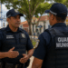 Dois guardas municipais fardados conversam em uma praça de cidade baiana.