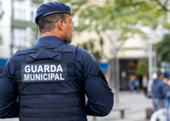 Guarda Municipal fardado visto de costas durante patrulha em área urbana, representando concurso público com inscrições abertas.