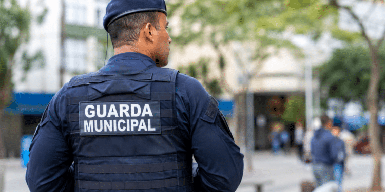 Guarda Municipal fardado visto de costas durante patrulha em área urbana, representando concurso público com inscrições abertas até sexta-feira.