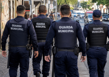 Quatro agentes da Guarda Municipal caminham por uma rua durante patrulhamento em área urbana.