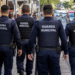 Quatro agentes da Guarda Municipal caminham por uma rua durante patrulhamento em área urbana.