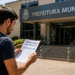Pessoa segurando edital de concurso público em frente à Prefeitura Municipal de Belo Vale-MG.