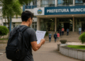 Candidato lendo edital de concurso público em frente à prefeitura municipal, com inscrições abertas e salários de até R$ 8.190.