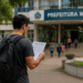 Candidato lendo edital de concurso público em frente à prefeitura municipal, com inscrições abertas e salários de até R$ 8.190.