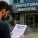 Candidato lendo edital de concurso público em frente à prefeitura municipal, relacionado a seleção na Bahia com quase 400 vagas.