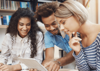 Candidatos estudando para concurso público com material de apoio e tablet em ambiente de preparação.