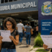 Candidatos lendo documentos de concurso público em frente a uma prefeitura municipal durante período de inscrições.