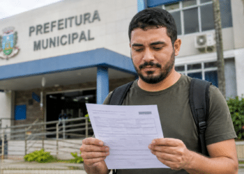 Homem lê documento de concurso em frente à Prefeitura Municipal, representando seleção com inscrições abertas na Paraíba.