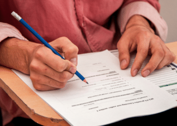 Pessoa preenchendo formulário de concurso público em carteira escolar, representando inscrições abertas para o Concurso Unificado no Piauí.