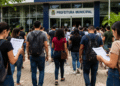 Pessoas caminhando em direção à prefeitura municipal com documentos de concurso público em mãos e celulares, representando oportunidades de empregos no serviço público.