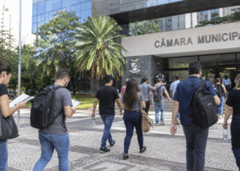 Candidatos caminham em direção a uma Câmara Municipal para participar de concurso público.