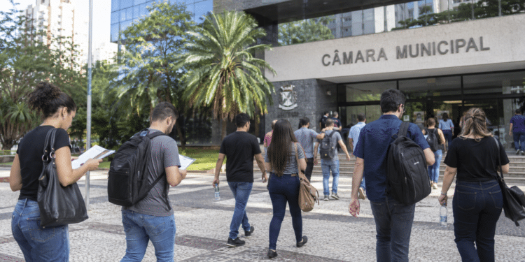 Candidatos caminham em direção a uma Câmara Municipal para participar de concurso público.
