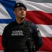 Guarda municipal uniformizado diante da bandeira da Bahia em imagem sobre concursos públicos no estado.