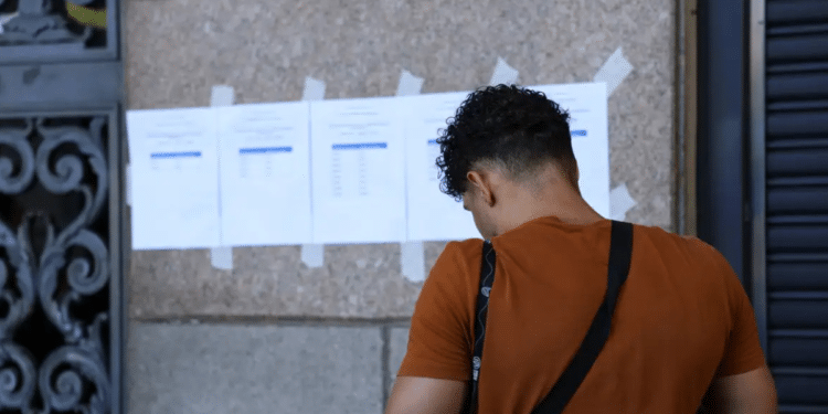 Pessoa consultando lista de aprovados em concurso do Ministério Público fixada na parede.