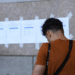 Pessoa consultando lista de aprovados em concurso do Ministério Público fixada na parede.