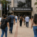 Candidatos caminham em direção à prefeitura com mochilas e documentos de concurso público.