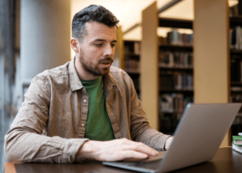Homem estudando para concurso público utilizando notebook em uma biblioteca.