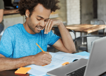 Candidato estuda com notebook e material impresso para concursos de prefeituras com vagas de nível médio.
