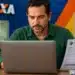 Homem utilizando um notebook e segurando um DARF do Imposto de Renda 2026, em referência à consulta ao terceiro lote da restituição.