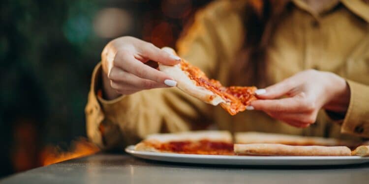 Pessoa pegando uma fatia de pizza, tema ligado à taxa de serviço e aos direitos do consumidor no Dia da Pizza