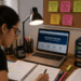 Pessoa estudando para concurso público com notebook, livros e anotações.