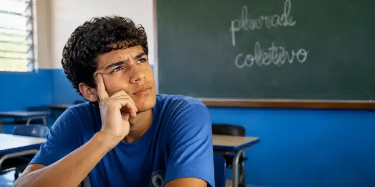 Estudante pensativo em sala de aula, com quadro ao fundo contendo as palavras “plural” e “coletivo” escritas, representando a diferença entre os conceitos da língua portuguesa.