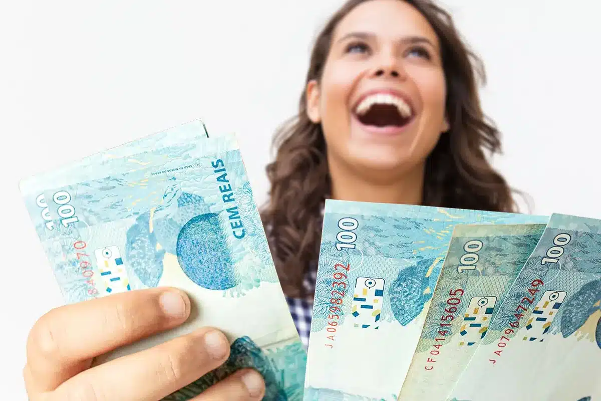 13º salário em 2026 - Direito ao benefício Pessoa segurando notas de real e sorrindo, em referência ao direito ao 13º salário em 2026.