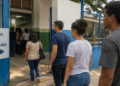 Grupo de eleitores em fila diante de uma placa indicando local de votação