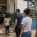 Grupo de eleitores em fila diante de uma placa indicando local de votação