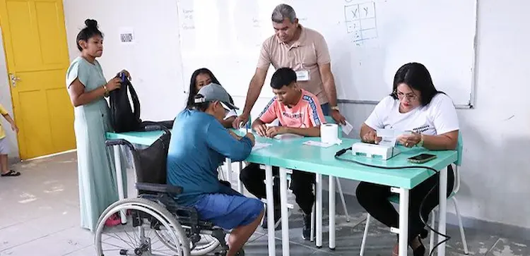 Seções acessíveis garantem inclusão nas Eleições 2026 Pessoa cadeirante recebe atendimento de mesários em seção eleitoral.