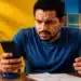Contribuinte consulta o celular e documentos do Imposto de Renda após erro na chave Pix impedir o recebimento da restituição.