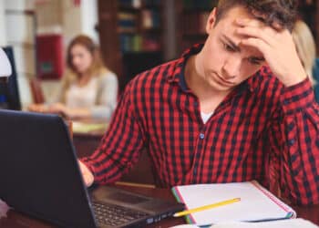 Estudante preocupado diante do notebook, ligado à escolha do curso superior por motivos financeiros