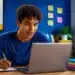 Jovem estudante utiliza notebook e faz anotações, representando os exercícios e simulados gratuitos oferecidos pelo MEC Enem.