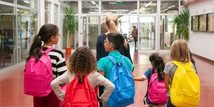 Estudantes com mochilas caminham dentro da escola.