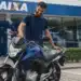 Homem ao lado de uma motocicleta nova em frente a uma agência da Caixa, representando o financiamento de motos pelo Move Brasil.
