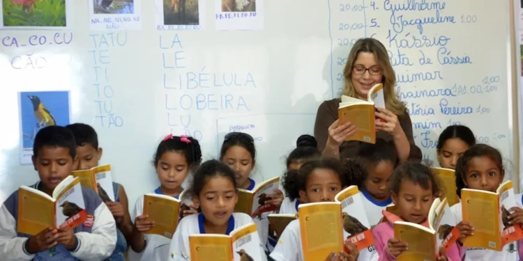 Professora conduz atividade de leitura com estudantes em sala de aula durante iniciativa de formação educacional.