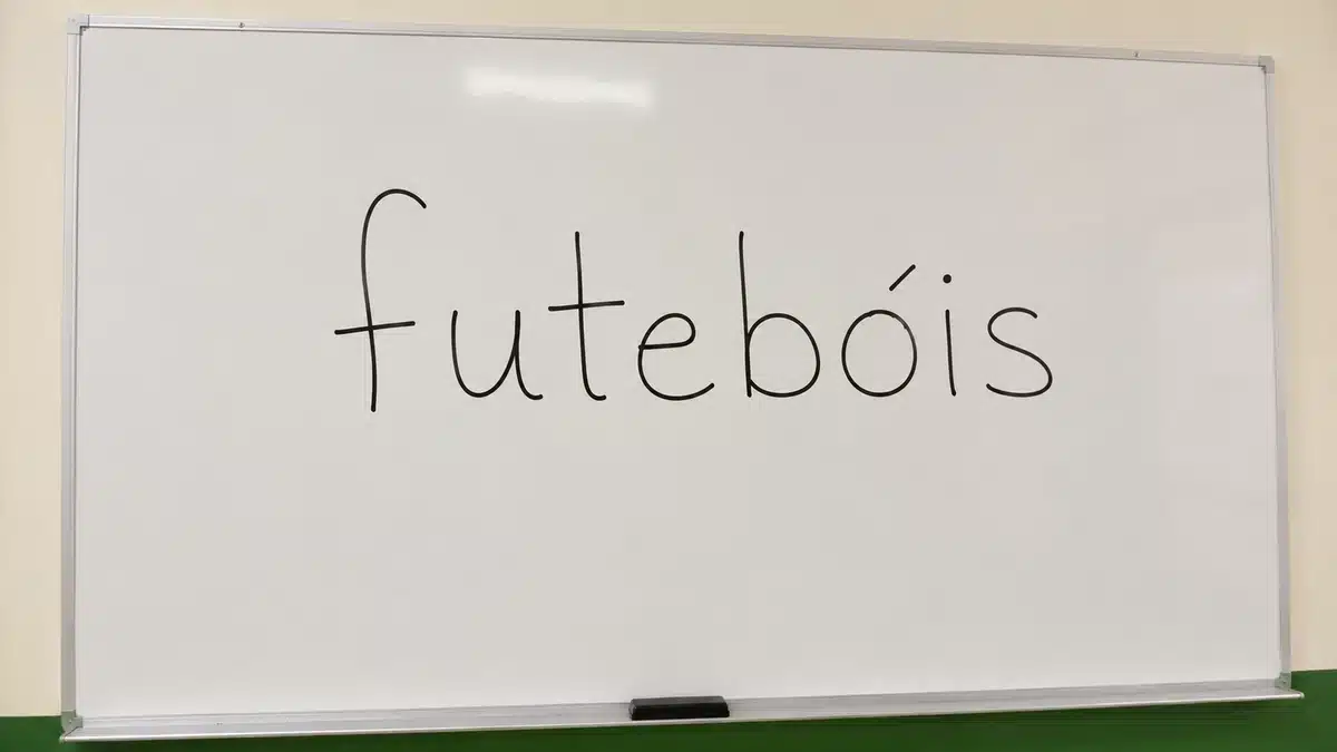 Futebóis - Palavra com acento agudo Palavra “futebóis” escrita em quadro branco para explicar o uso do acento agudo no plural de futebol.