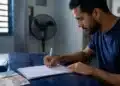 Jovem brasileiro assina documentos relacionados ao Fies Empreendedor, ilustrando a cobrança de juros durante o período de carência.