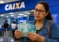 Mulher conferindo cédulas de R$ 100 em uma agência da Caixa, representando a liberação de valores esquecidos do PIS/Pasep.