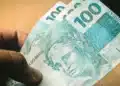 Pessoa segurando notas de R$ 100, ilustrando as regras da linha de crédito do Fies Empreendedor e do Desenrola Adimplentes.