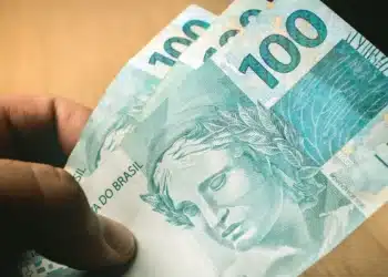 Pessoa segurando notas de R$ 100, ilustrando as regras da linha de crédito do Fies Empreendedor e do Desenrola Adimplentes.