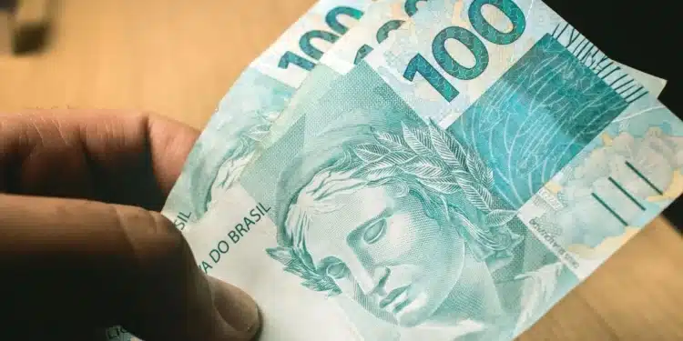 Pessoa segurando notas de R$ 100, ilustrando as regras da linha de crédito do Fies Empreendedor e do Desenrola Adimplentes.