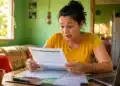 Mulher brasileira analisa documentos em casa, representando as mudanças no Cadastro Único para pessoas que moram sozinhas até 2027.