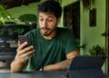 Homem olhando o celular à mesa, com um tablet à frente e um carro ao fundo, cena que representa as novidades do WhatsApp para o telefone, o tablet e o carro.